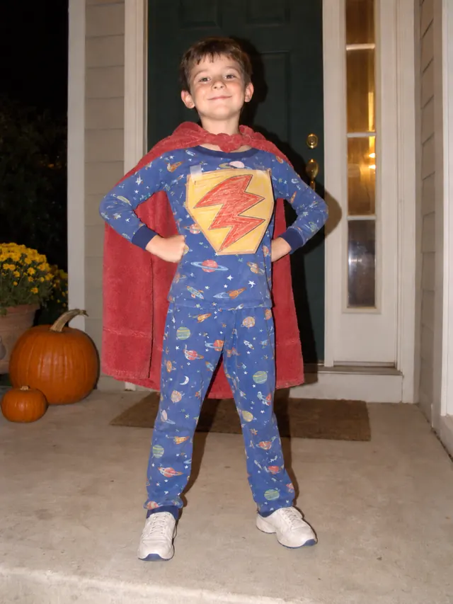 Boy in space pajamas with a red towel cape and a paper lightning bolt on his chest on a front porch