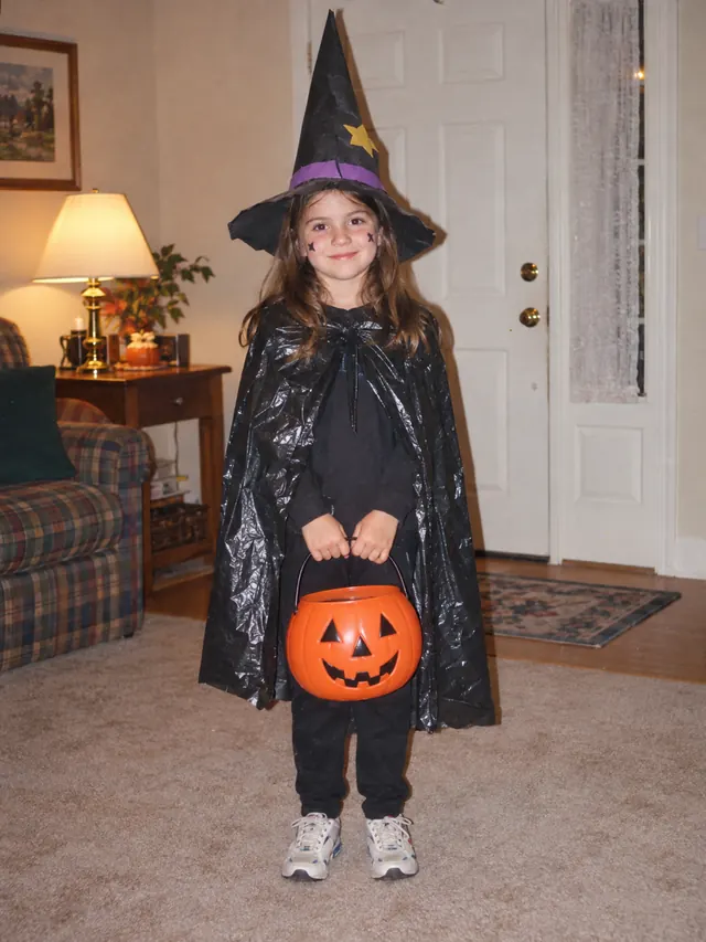 Seven-year-old girl in a homemade witch costume with a paper hat and black plastic cape in a living room